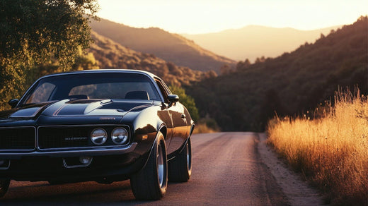 A vintage muscle car cruises along a picturesque road framed by vibrant landscapes